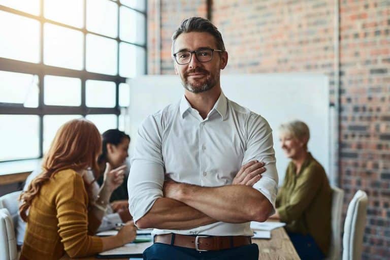 Formateur les bras croisés en formation devant ses stagiaires et souriant stagiaires derrière lui